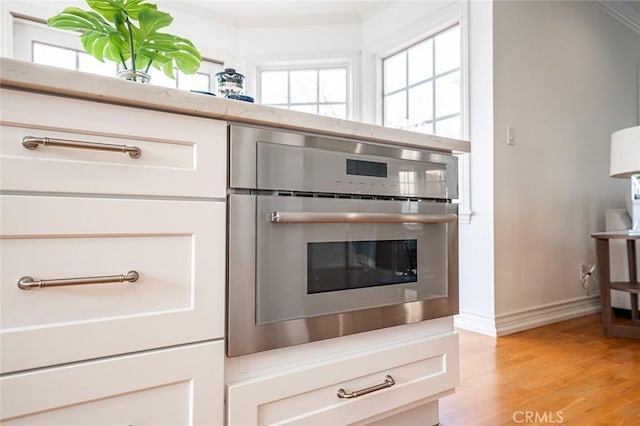 details featuring white cabinets, light wood-style flooring, stainless steel oven, and baseboards