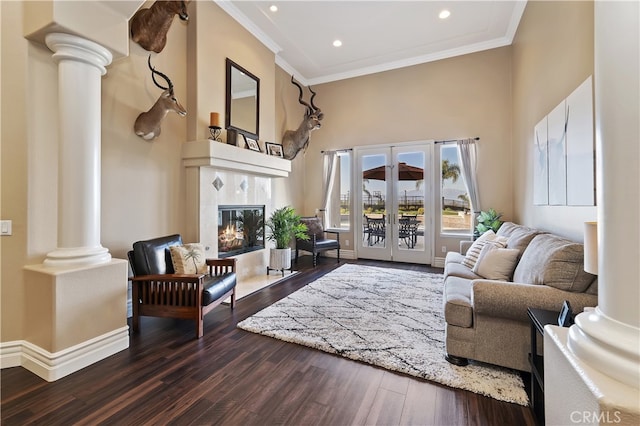 living area featuring a tile fireplace, dark wood-type flooring, ornamental molding, french doors, and ornate columns