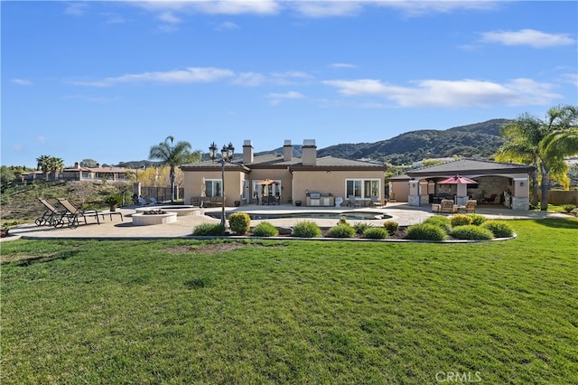 back of property featuring an outdoor fire pit, a mountain view, a gazebo, a lawn, and a patio area