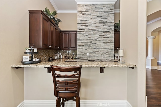 bar featuring arched walkways, decorative backsplash, ornamental molding, a bar, and ornate columns