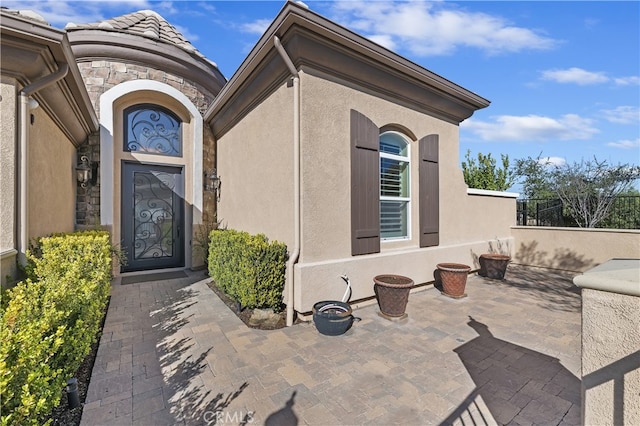 entrance to property featuring stone siding, a patio area, and stucco siding