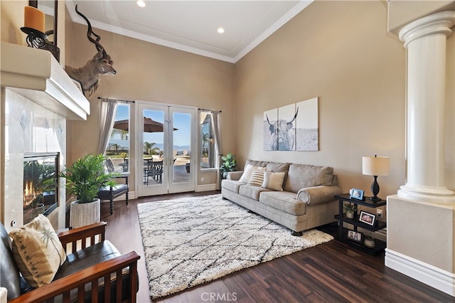 living room featuring ornamental molding, a high ceiling, dark wood finished floors, and decorative columns