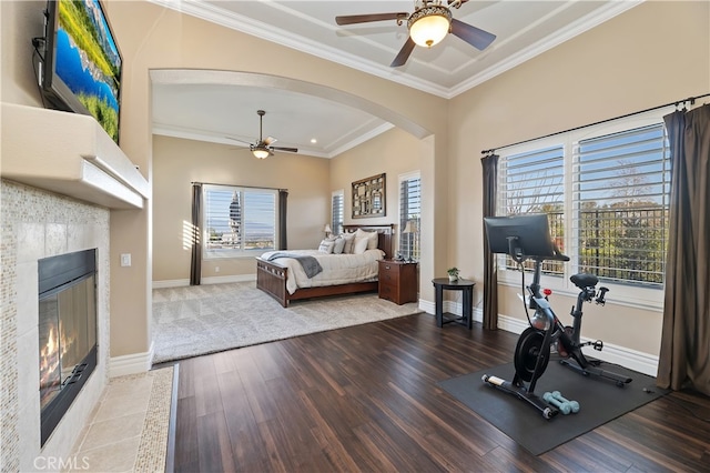 bedroom featuring a fireplace, arched walkways, crown molding, and wood finished floors