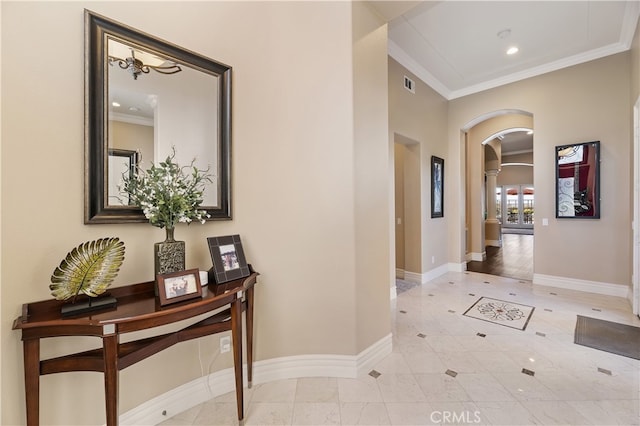 hallway featuring baseboards, visible vents, arched walkways, and crown molding