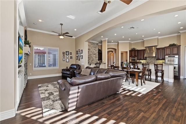 living room with arched walkways, a ceiling fan, dark wood-type flooring, ornamental molding, and baseboards