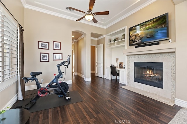 exercise room featuring dark wood-style floors, arched walkways, a fireplace, crown molding, and baseboards