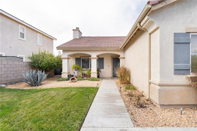 property entrance featuring a chimney, fence, a lawn, and stucco siding