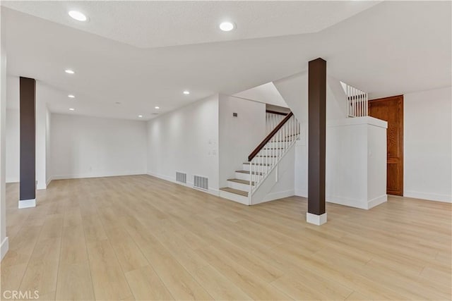 finished below grade area with light wood-style flooring, stairs, visible vents, and recessed lighting