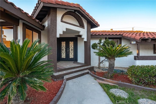 view of exterior entry featuring stucco siding, french doors, and a tiled roof