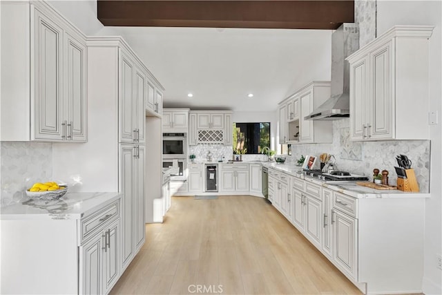 kitchen with stainless steel appliances, wall chimney range hood, white cabinetry, and light stone counters