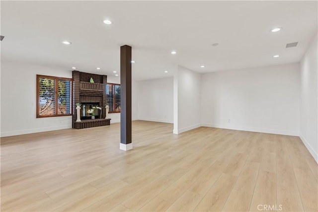 below grade area with baseboards, light wood finished floors, a brick fireplace, and recessed lighting