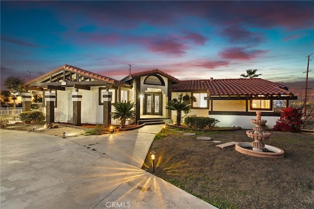 mediterranean / spanish-style house featuring a tiled roof, fence, french doors, and stucco siding