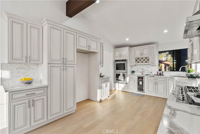 kitchen featuring lofted ceiling with beams, light wood-style flooring, beverage cooler, white cabinets, and light stone countertops