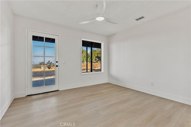 empty room featuring a ceiling fan, visible vents, light wood-style flooring, and baseboards