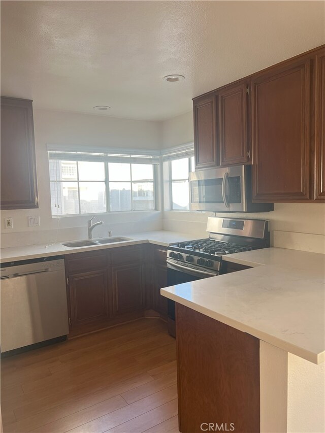 kitchen featuring a peninsula, stainless steel appliances, light countertops, light wood-type flooring, and a sink