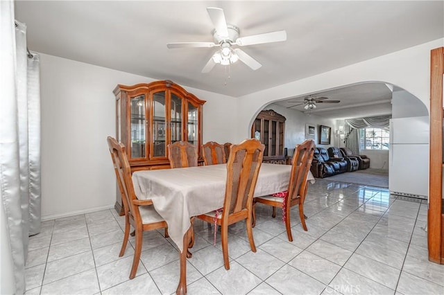 dining room with arched walkways, light tile patterned flooring, a ceiling fan, and baseboards