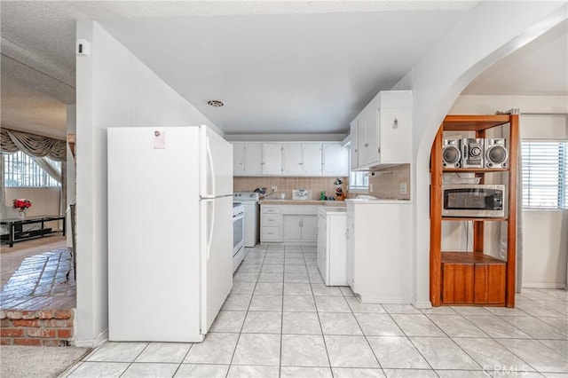 kitchen featuring arched walkways, white appliances, white cabinetry, light countertops, and decorative backsplash