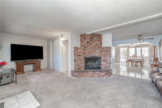 living room featuring arched walkways, a fireplace, light tile patterned floors, light carpet, and a textured ceiling