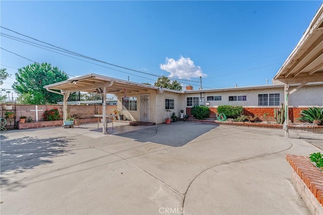 rear view of house featuring a patio area, fence, and stucco siding