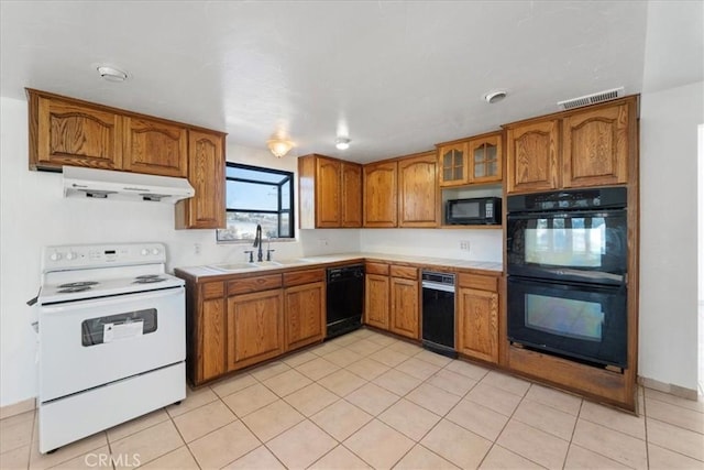 kitchen with brown cabinetry, glass insert cabinets, under cabinet range hood, light countertops, and black appliances