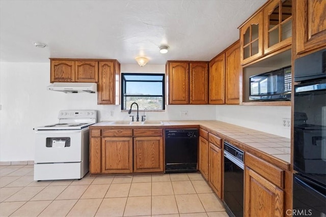 kitchen with tile counters, brown cabinetry, a sink, under cabinet range hood, and black appliances