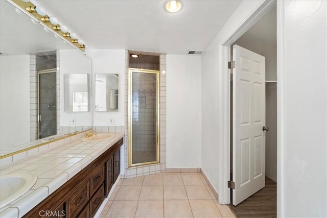 bathroom with double vanity, a stall shower, visible vents, tile patterned flooring, and a sink