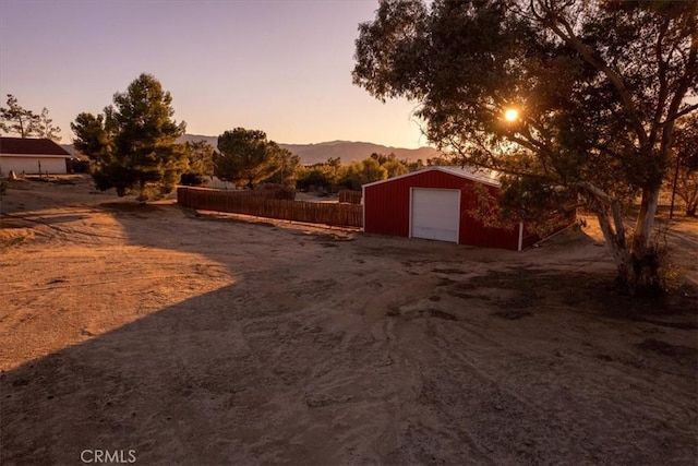 yard at dusk featuring an outbuilding, a mountain view, a detached garage, fence, and driveway