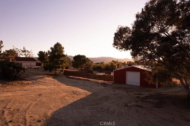 yard at dusk featuring an outbuilding, a mountain view, and fence