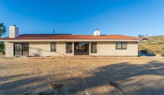 rear view of house featuring a tiled roof, a chimney, and stucco siding