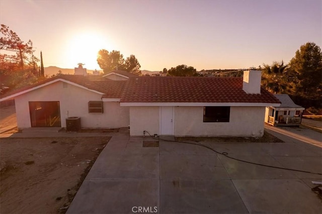 view of front of home with cooling unit, a tiled roof, stucco siding, a chimney, and a patio area