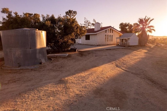 exterior space with driveway, stucco siding, a chimney, and an outbuilding