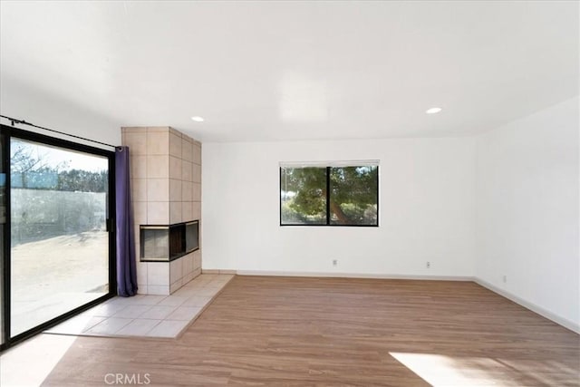 empty room with light wood-style floors, recessed lighting, baseboards, and a tile fireplace