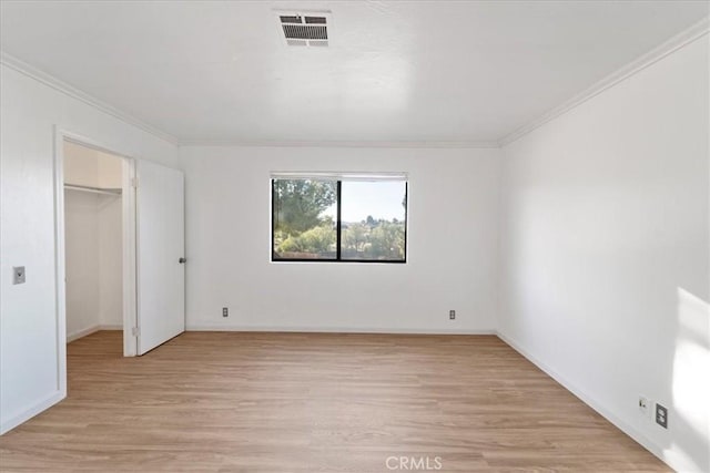 unfurnished bedroom featuring a spacious closet, light wood finished floors, visible vents, and crown molding