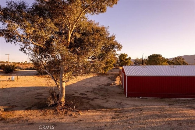 yard at dusk with a pole building, a mountain view, and an outbuilding