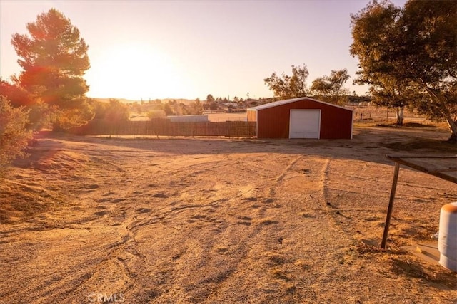 yard at dusk featuring a garage, a rural view, an outbuilding, and fence