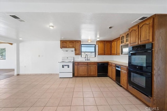 kitchen featuring brown cabinets, light countertops, glass insert cabinets, a sink, and black appliances