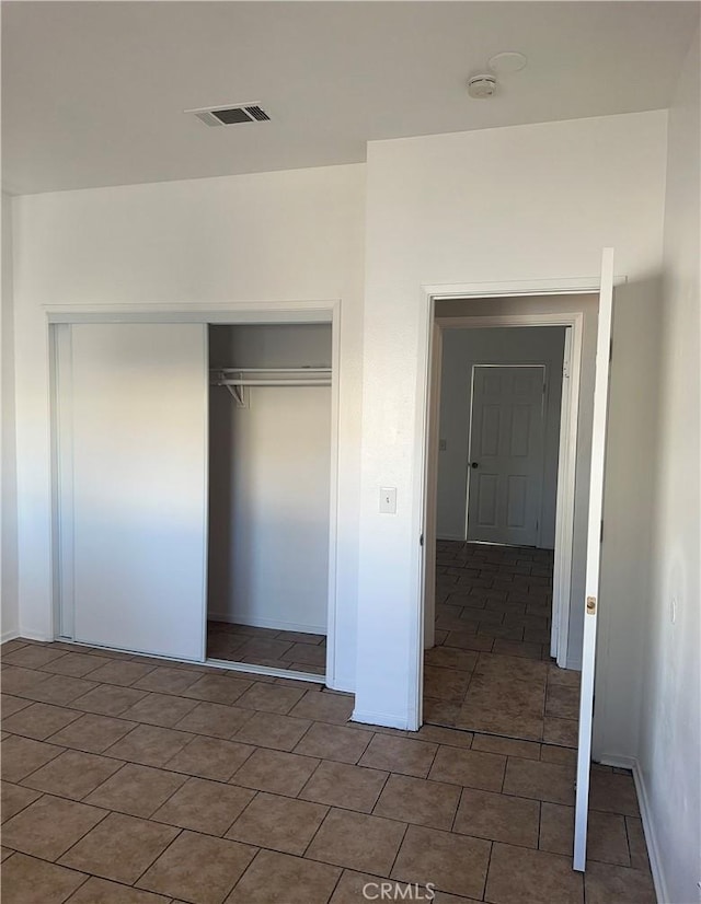 unfurnished bedroom with dark tile patterned flooring, a closet, and visible vents