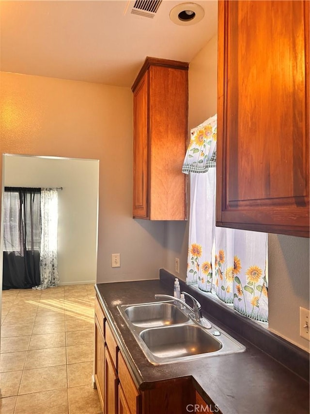 kitchen with light tile patterned floors, a sink, visible vents, brown cabinets, and dark countertops