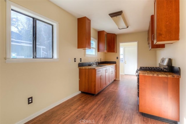 kitchen featuring dark wood-style flooring, brown cabinetry, stainless steel range with gas stovetop, a sink, and baseboards