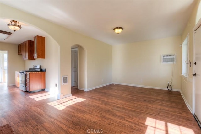 unfurnished living room with dark wood-type flooring, arched walkways, a wall mounted air conditioner, and baseboards