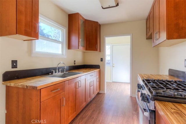 kitchen featuring wooden counters, brown cabinetry, dark wood-type flooring, a sink, and stainless steel gas range oven