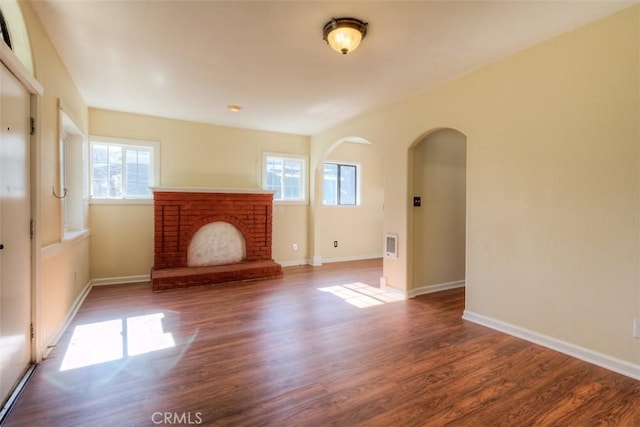 unfurnished living room featuring dark wood-style floors, a fireplace, arched walkways, and baseboards