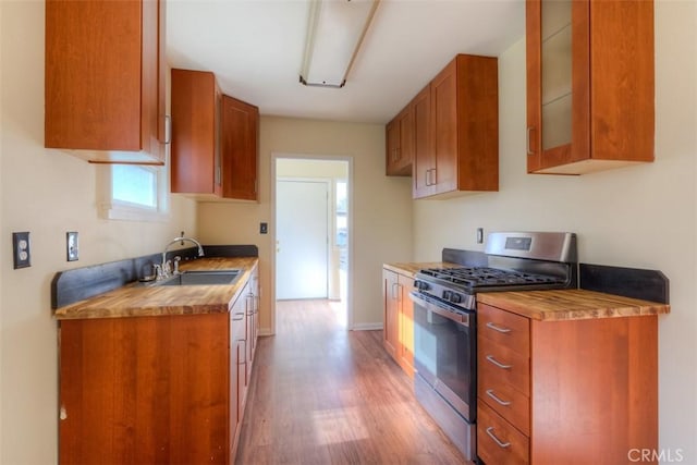 kitchen with glass insert cabinets, brown cabinetry, stainless steel gas stove, and a sink