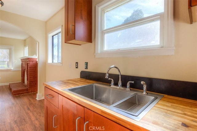 kitchen featuring arched walkways, dark wood-style flooring, a fireplace, brown cabinetry, and a sink