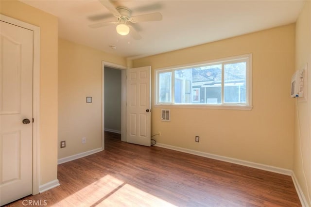 unfurnished bedroom with ceiling fan, a wall mounted AC, baseboards, and wood finished floors