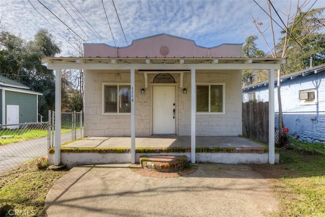 bungalow-style house featuring a porch, concrete block siding, fence, and metal roof