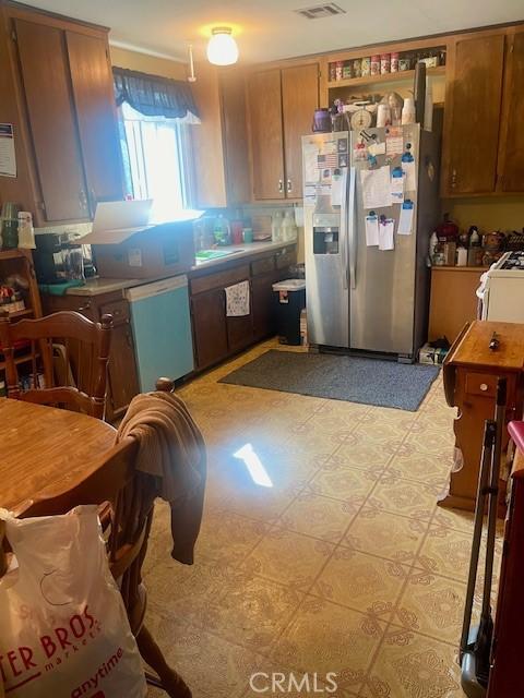 kitchen featuring gas range gas stove, visible vents, light countertops, stainless steel fridge with ice dispenser, and brown cabinetry