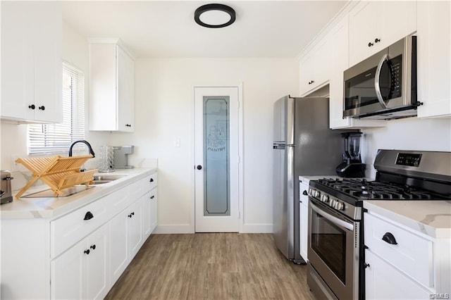 kitchen featuring white cabinets, light wood-type flooring, stainless steel appliances, and light countertops