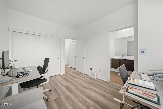 office area with light wood-style floors, baseboards, and a sink