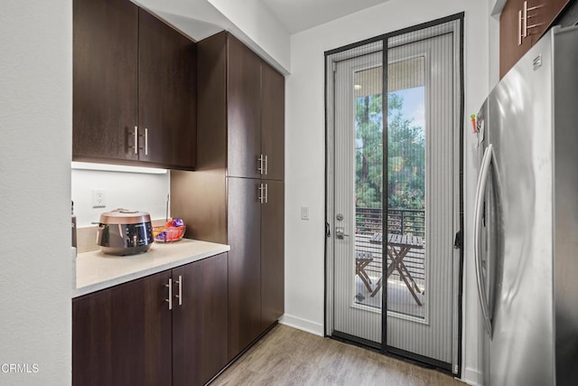 kitchen with dark brown cabinetry, light countertops, freestanding refrigerator, light wood finished floors, and modern cabinets